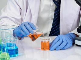 estudiante científico asiático en un laboratorio de mezcla de reactivos en un laboratorio de investigación científica con tubos de ensayo de varios tamaños y microscopios. sobre la mesa en el fondo blanco de laboratorio de química de laboratorio. foto