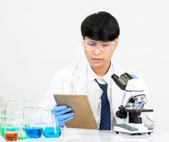 estudiante científico asiático en un laboratorio de mezcla de reactivos en un laboratorio de investigación científica con tubos de ensayo de varios tamaños y microscopios. sobre la mesa en el fondo blanco de laboratorio de química de laboratorio. foto