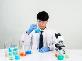 estudiante científico asiático en un laboratorio de mezcla de reactivos en un laboratorio de investigación científica con tubos de ensayo de varios tamaños y microscopios. sobre la mesa en el fondo blanco de laboratorio de química de laboratorio. foto