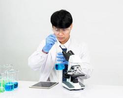 estudiante científico asiático en un laboratorio de mezcla de reactivos en un laboratorio de investigación científica con tubos de ensayo de varios tamaños y microscopios. sobre la mesa en el fondo blanco de laboratorio de química de laboratorio. foto