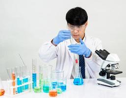 estudiante científico asiático en un laboratorio de mezcla de reactivos en un laboratorio de investigación científica con tubos de ensayo de varios tamaños y microscopios. sobre la mesa en el fondo blanco de laboratorio de química de laboratorio. foto