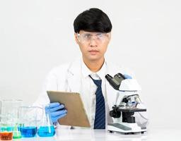 estudiante científico asiático en un laboratorio de mezcla de reactivos en un laboratorio de investigación científica con tubos de ensayo de varios tamaños y microscopios. sobre la mesa en el fondo blanco de laboratorio de química de laboratorio. foto