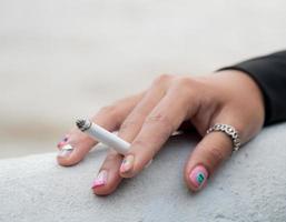 Primer plano mano mujer joven adolescente asia una persona que lleva una camisa negra mantenga fumar cigarrillo color blanco de pie al aire libre junto a la pared foto