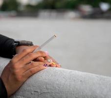 Primer plano mano mujer adolescente joven asia una persona que lleva una camisa negra mantenga fumar cigarrillo color blanco de pie al aire libre junto a la pared foto