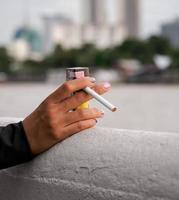 Primer plano mano mujer adolescente joven asia una persona que lleva una camisa negra mantenga fumar cigarrillo color blanco de pie al aire libre junto a la pared foto