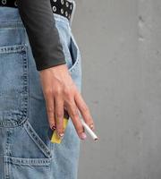 Closeup hand woman teen young asia one person wearing a black shirt hold smoking cigarette white color standing outdoor by the wall photo