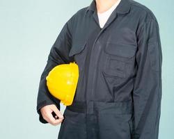 Worker standing in blue coverall holding yellow hardhat photo