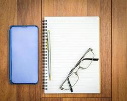 Top view image of open notebook with blank page and cellphone on wooden table photo