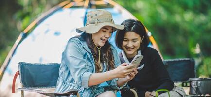 Asian pretty woman and friend use smartphone selfie on camping photo