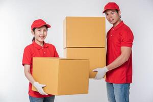 Image of a happy young delivery man in red cap blank t-shirt uniform standing with empty brown cardboard box isolated on light gray background studio photo