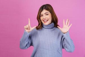 Portrait of Happy young woman pointing up with finger number seven isolated over pink background photo