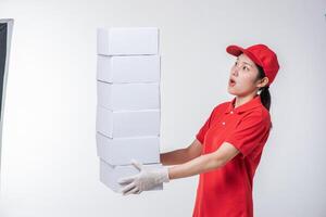 Image of a happy young delivery man in red cap blank t-shirt uniform standing with empty white cardboard box isolated on light gray background studio photo