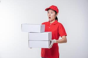 imagen de un joven repartidor con uniforme de camiseta en blanco con gorra roja de pie con una caja de cartón blanca vacía aislada en un estudio de fondo gris claro foto