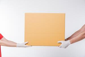 Image of a happy young delivery man in red cap blank t-shirt uniform standing with empty brown cardboard box isolated on light gray background studio photo