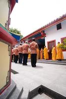 Bandung, Indonesia, 2020 - The monks in orange rob standing in order while praying to the god at the altar inside the Buddha temple photo