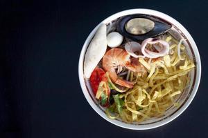 fideos tailandeses tom yam comida de mar mee krob con carne de camarones, mariscos, calamares y bolas de carne en un piso de madera de color negro. foto