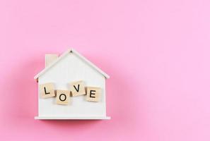 flat lay of wooden model house with wooden letters L O V E on it  on pink  background. dream house , home of love, strong relationship, valentines. photo