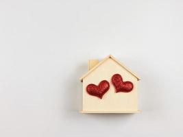 endecha plana de casa modelo de madera con dos corazones rojos brillantes aislados en fondo blanco. casa de ensueño, hogar de amor, relación fuerte, san valentín. foto