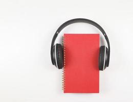 endecha plana de cuaderno rojo o diario o planificador cubierto con auriculares aislados sobre fondo blanco con espacio de copia. concepto de audiolibro o podcast. foto
