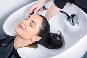 peluquero profesional lavando el cabello de una mujer joven en un salón de belleza foto