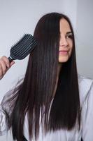 Young woman combing her long dark hair with a comb in a beauty salon photo