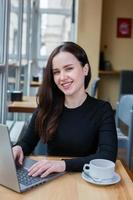 Beautiful businesswoman working on laptop in coffee shop. Female freelancer connecting to internet via computer. Blogger or journalist writing new article. photo