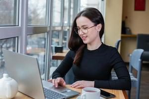 Beautiful businesswoman working on laptop in coffee shop. Female freelancer connecting to internet via computer. Blogger or journalist writing new article. photo