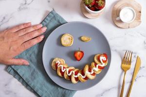 Small pancakes with strawberries in the original serving in the form of a smiley face. Top view. Flat lay photo