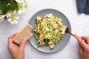 Salad of fresh vegetables and crab sticks in a plate with female hands. The concept of healthy eating photo