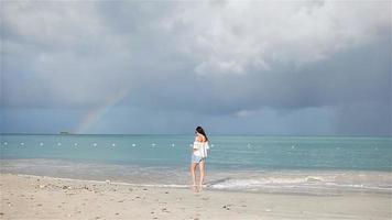 Young beautiful woman on tropical seashore with rainbow on background. Happy girl relaxing at white sand tropical beach video