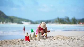 entzückendes kleines mädchen, das im strandurlaub mit spielzeug spielt. Kind, das eine Sandburg an der Küste baut video