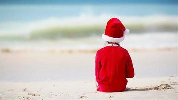 Back view of adorable girl in Christmas hat on the beach during Xmas vacation video