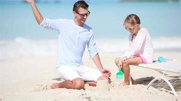 Father and little daughter making sand castle at tropical beach video