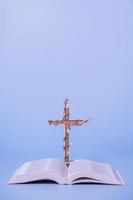 Cross decorated flowers with Holy Bible on purple background. Easter holiday minimalistic concept photo