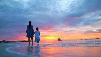niña y madre feliz silueta en la hermosa puesta de sol en la playa. colores asombrosos en el horizonte video