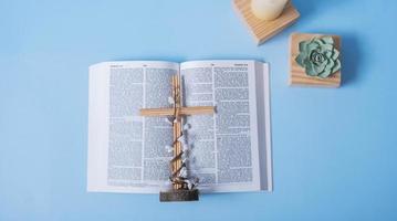 Open Holy Bible with candles and decorative flowers on blue background photo