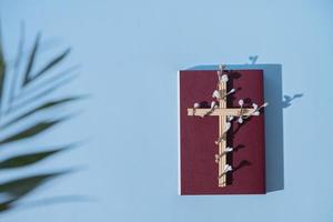 Cross decorated flowers with Holy Bible on blue background. Easter holiday minimalistic concept photo