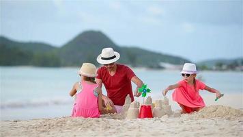 pai e filhos fazendo castelo de areia na praia tropical video