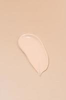 Foundation makeup cream smear smudge on beige background. Concealer swatch. Creamy beauty product texture photo