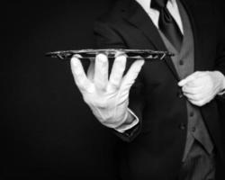 Close Up of Butler or Waiter in Dark Suit and White Gloves Holding Silver Serving Tray on Black Background. Elegant and Professional Service. photo