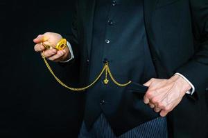 Portrait of Successful Businessman in Dark Suit Holding Pocket Watch on Black Background. Classic Gentleman in Vintage Fashion. photo