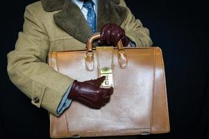 Portrait of Man in Brown Fur Overcoat and Leather Gloves Working the Combination to Attache Case on Black Background. Concept of Secret Agent Spy Hero Film Noir. photo