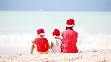 Happy beautiful family in red Santa hats on a tropical beach celebrating Christmas. Mom and kids enjoy xmas holidays video