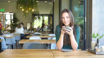 mujer joven sentada en un café al aire libre bebiendo café. retrato de niña feliz con taza de café video