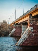 antiguo puente sobre el río con pilares de piedra. flujo rápido de agua en primavera. vista del atardecer foto