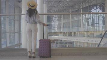jovem mulher com bagagem no aeroporto internacional andando com sua bagagem. passageiro da companhia aérea em um saguão do aeroporto à espera de aeronaves de voo video