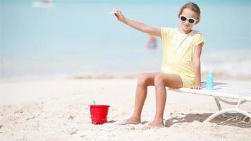 Happy little girl with toy airplane in hands on white sandy beach. Kid play with toy on the beach video