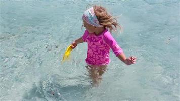 Little adorable girl playing frisbee during tropical vacation. Kid have fun with beach toy in shallow water video