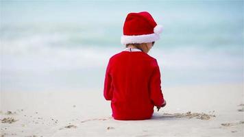 Back view of adorable girl in Christmas hat on white beach during Xmas vacation video