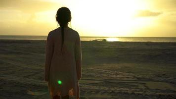 Adorable happy little girl walking on white beach at sunset video